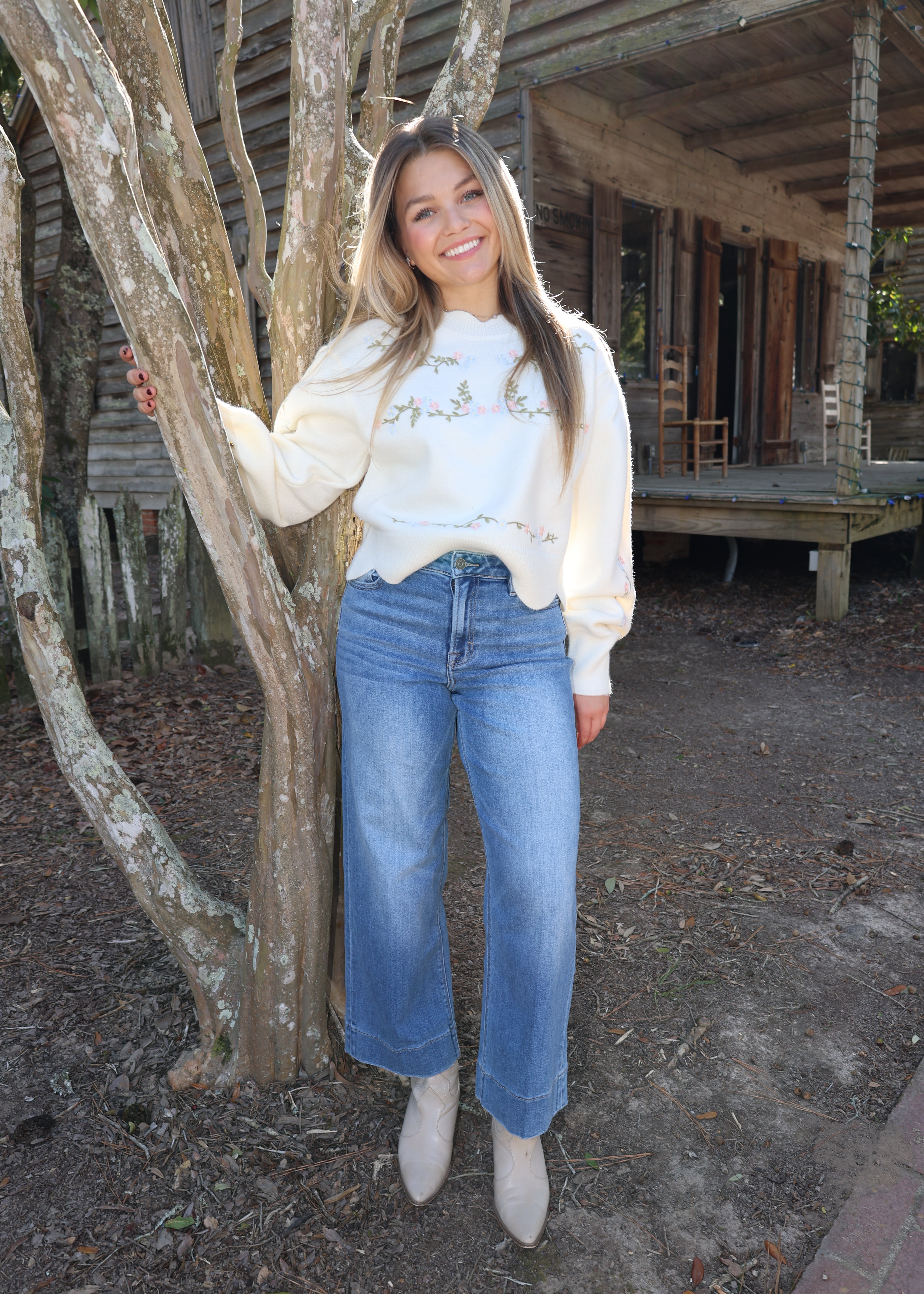 Person wearing a white sweater and blue jeans standing near wooden beams.