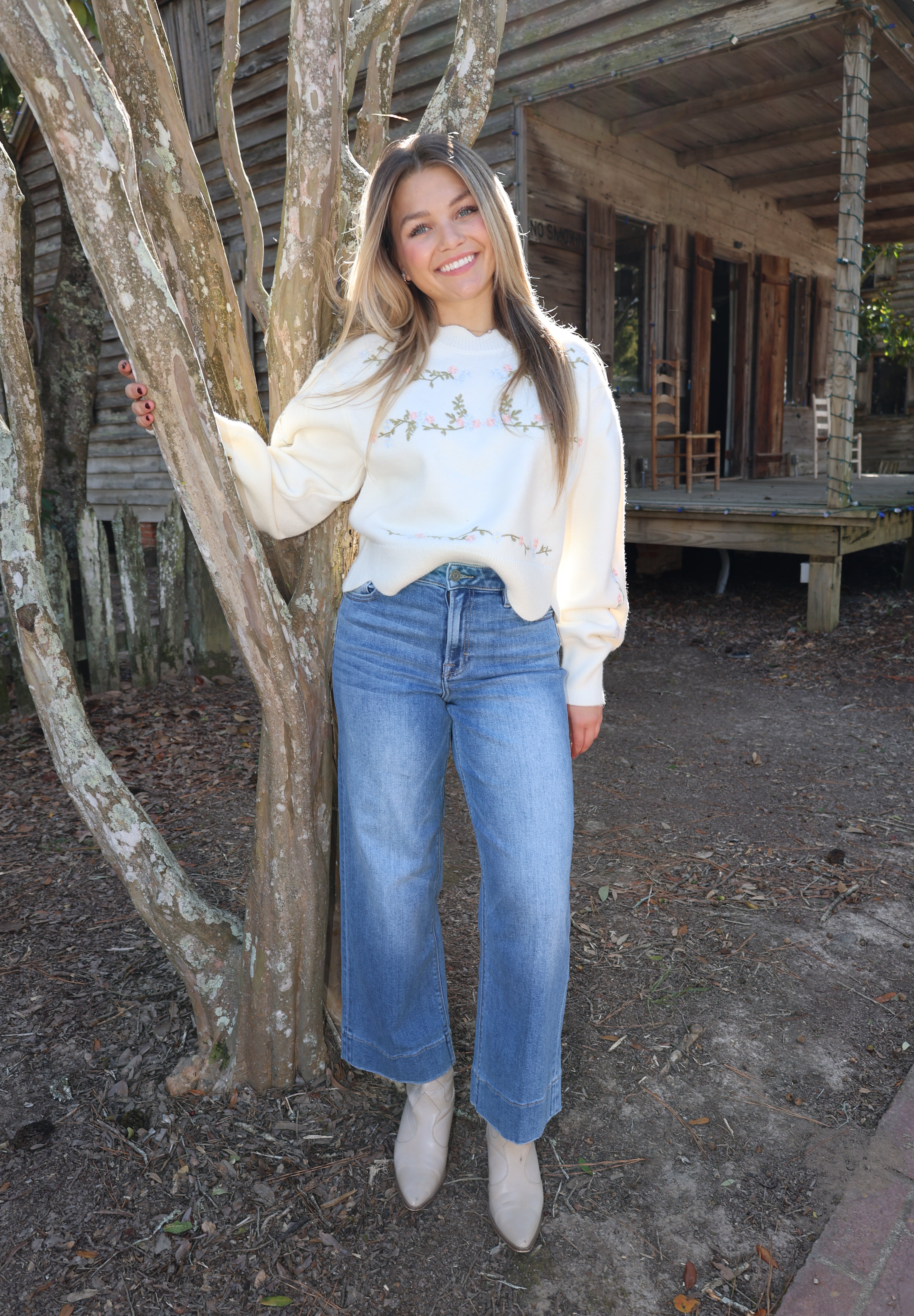 Person wearing a white sweater and blue jeans standing near wooden beams.