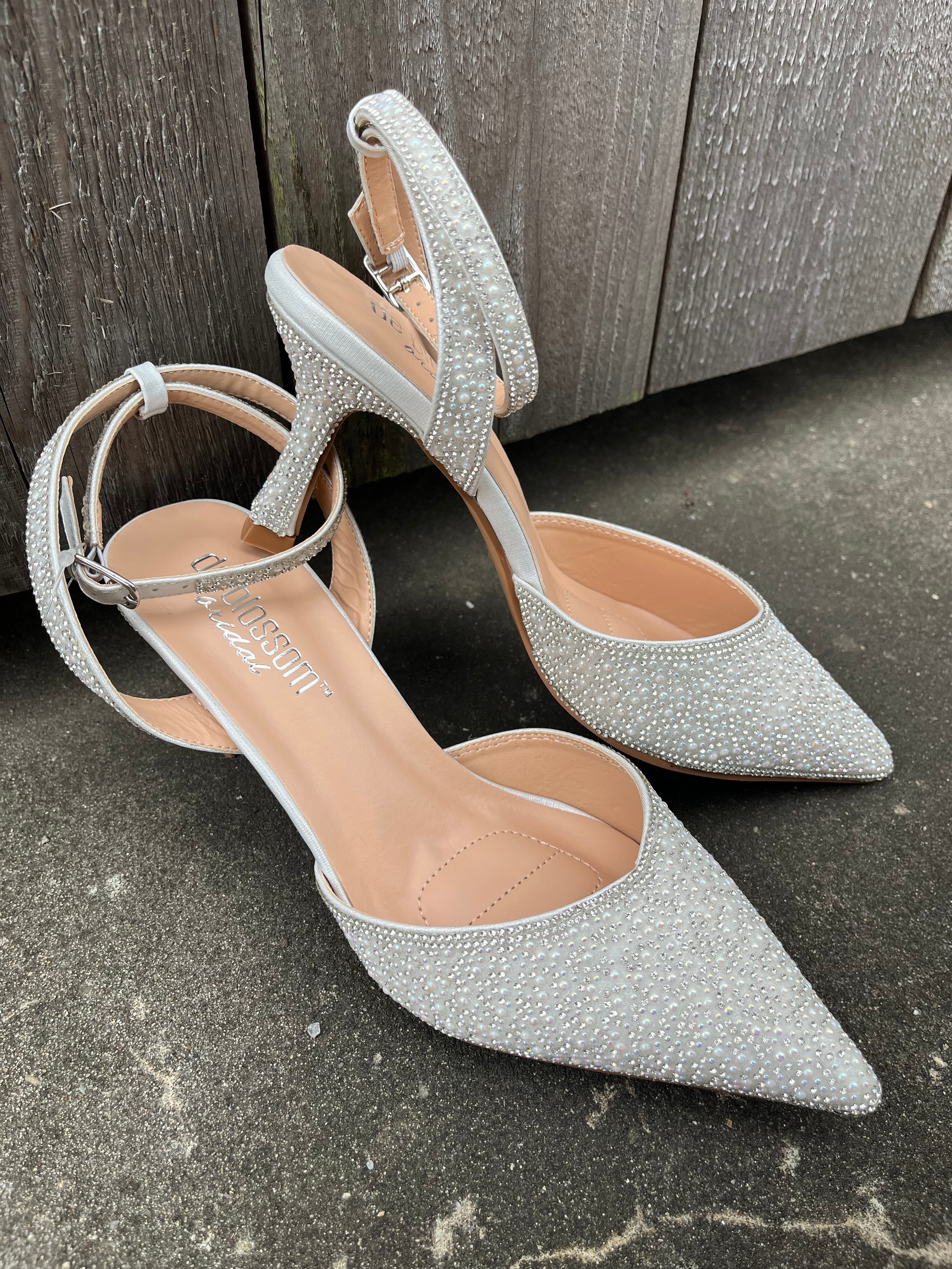 A pair of white pearl-heeled sandals with ankle straps, displayed on a wooden surface.