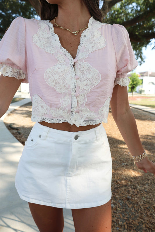 Person wearing a pink lace top and white skirt outdoors