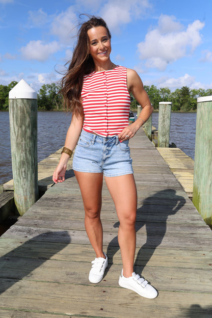 Woman standing on a wooden dock by a body of water with a blue sky and clouds in the background.