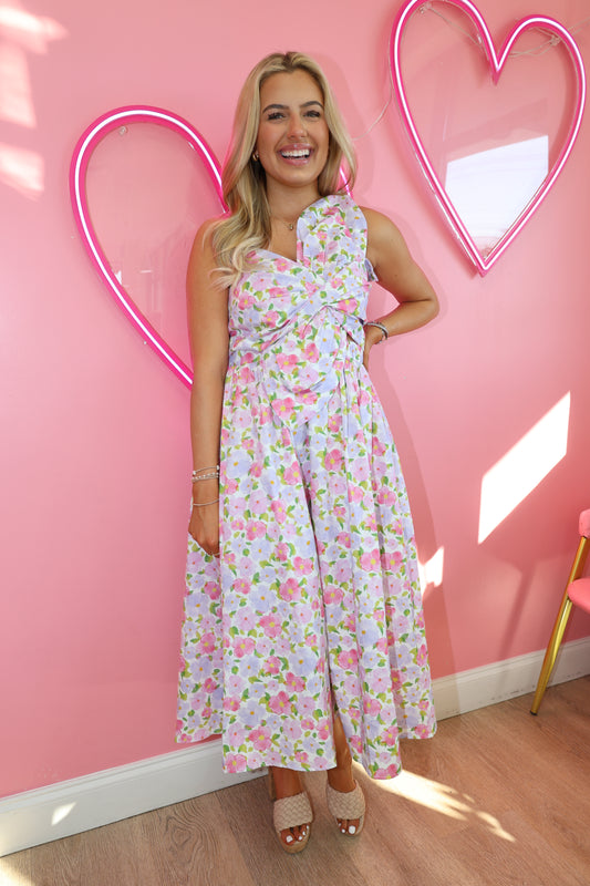 Woman in a floral dress standing on a pink floor with a neon heart light.
