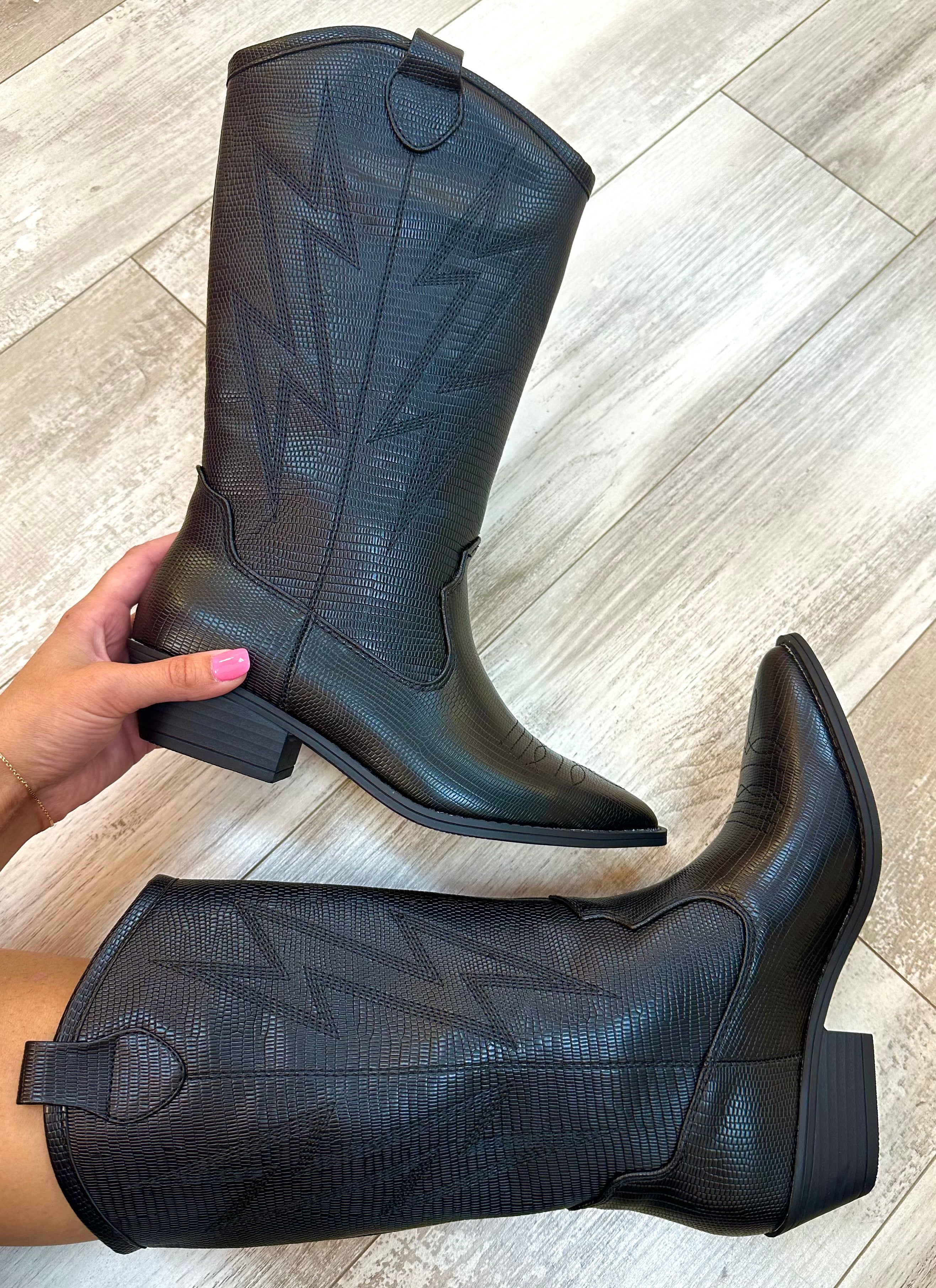 A pair of black, faux leather boots with a high heel and pointed toe, displayed against a textured background.