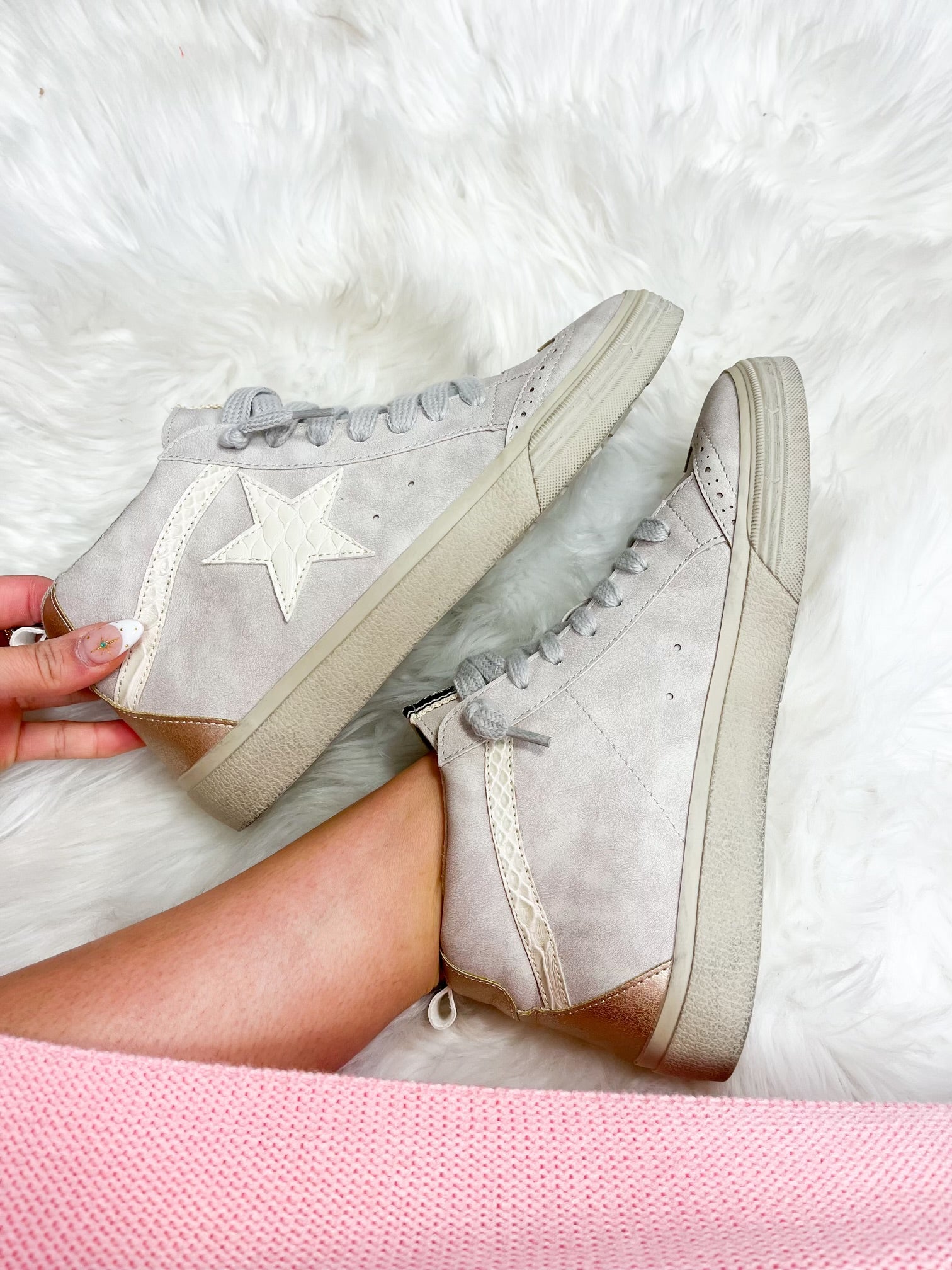 A pair of light grey sneakers with a star design on the white tongue, placed on a fluffy white surface.