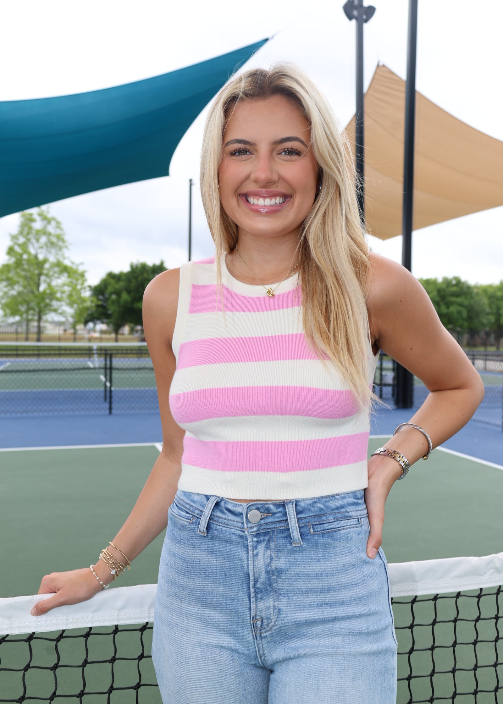 Woman in striped tank top and jeans standing on a tennis court