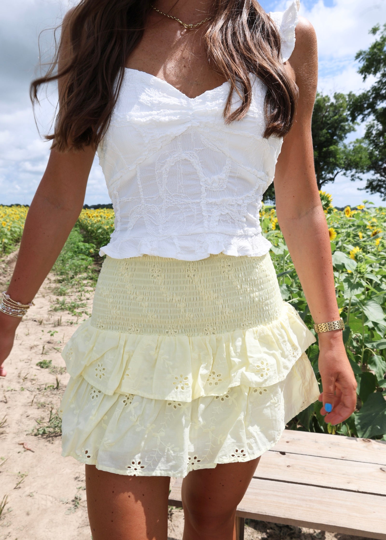 Woman wearing a white top and yellow skirt standing in a field with sunflowers.
