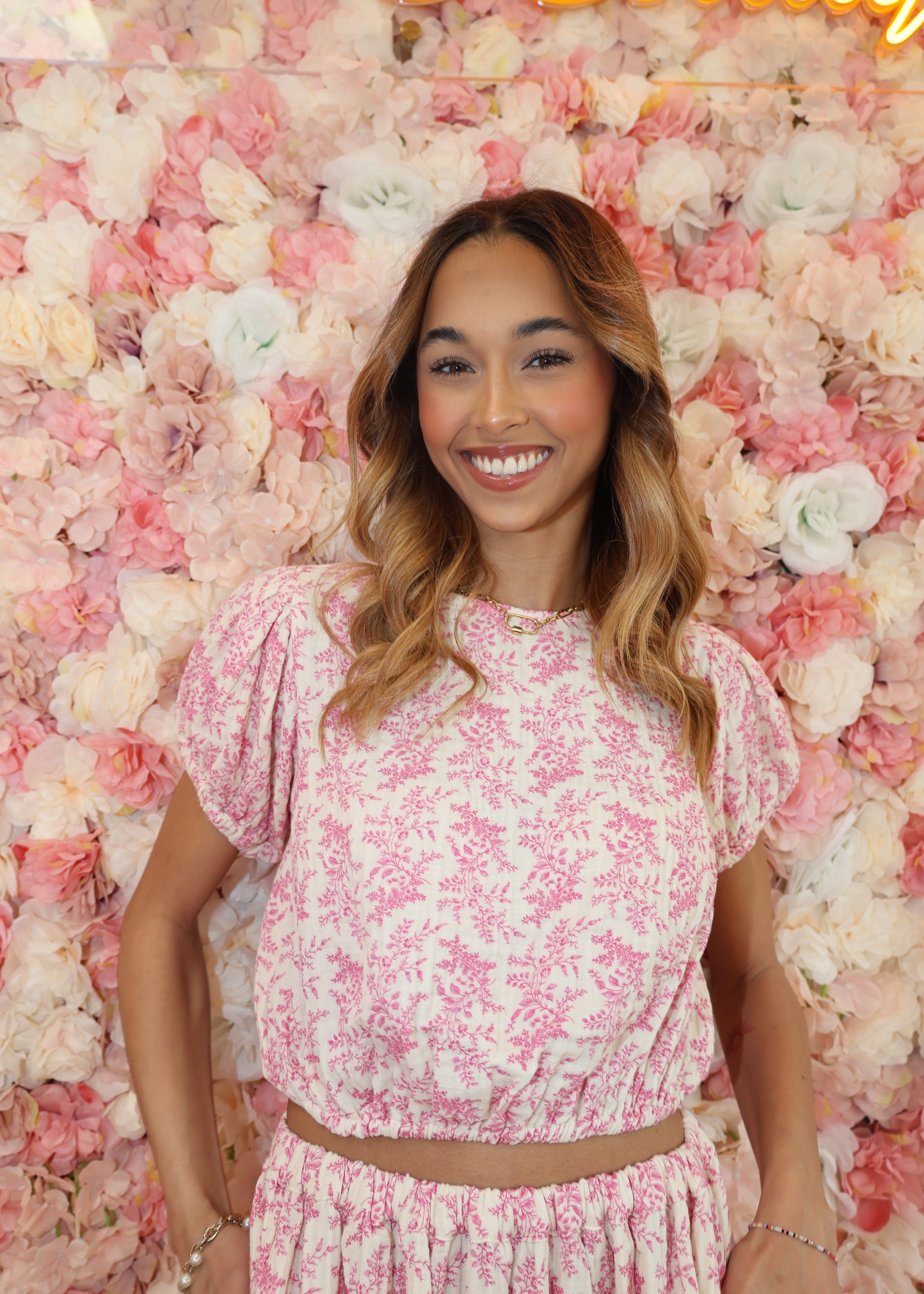 Woman in a pink floral dress lying on a bed of flowers with a neon sign in the corner.