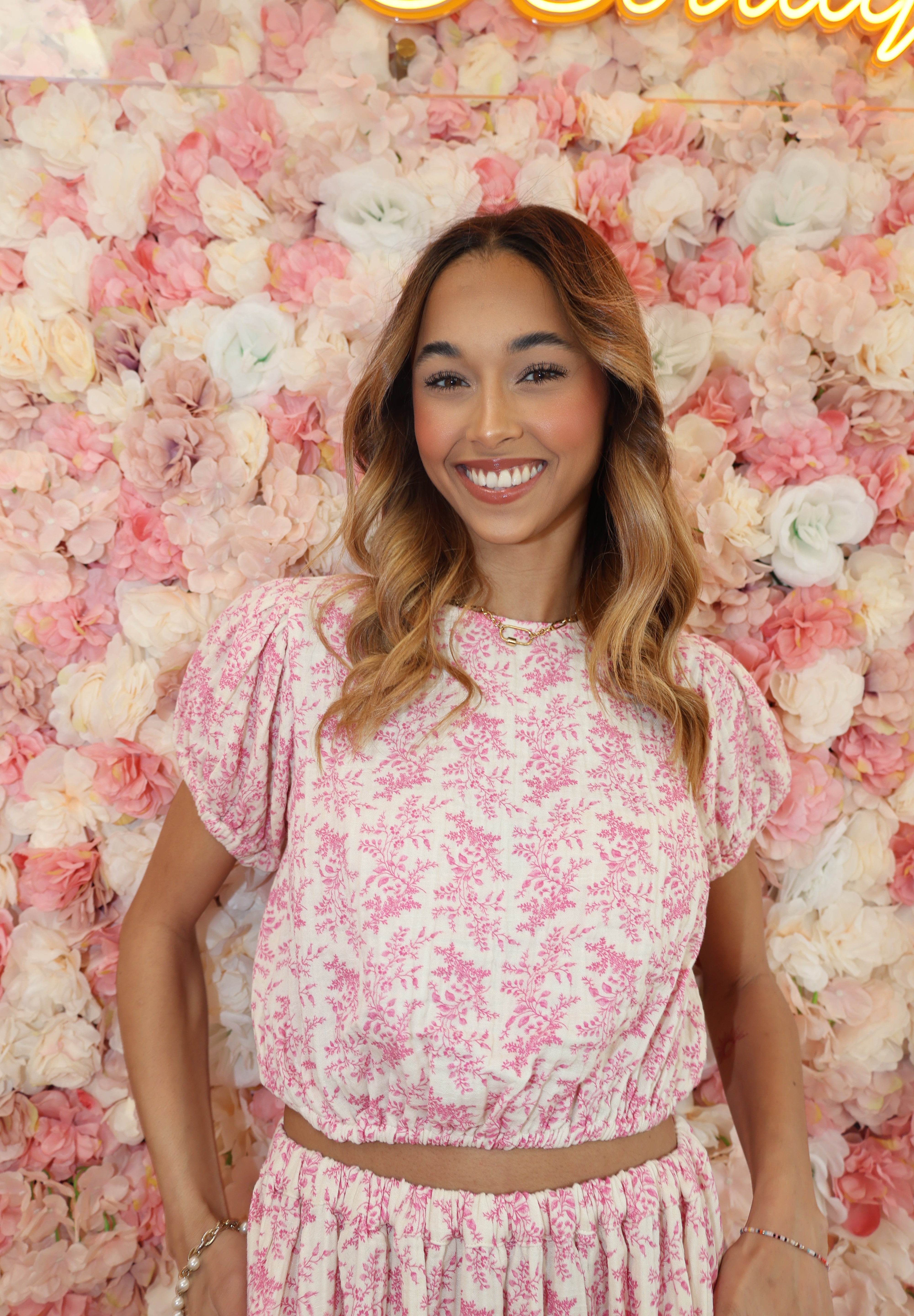 Woman in a pink floral dress lying on a bed of flowers with a neon sign in the corner.