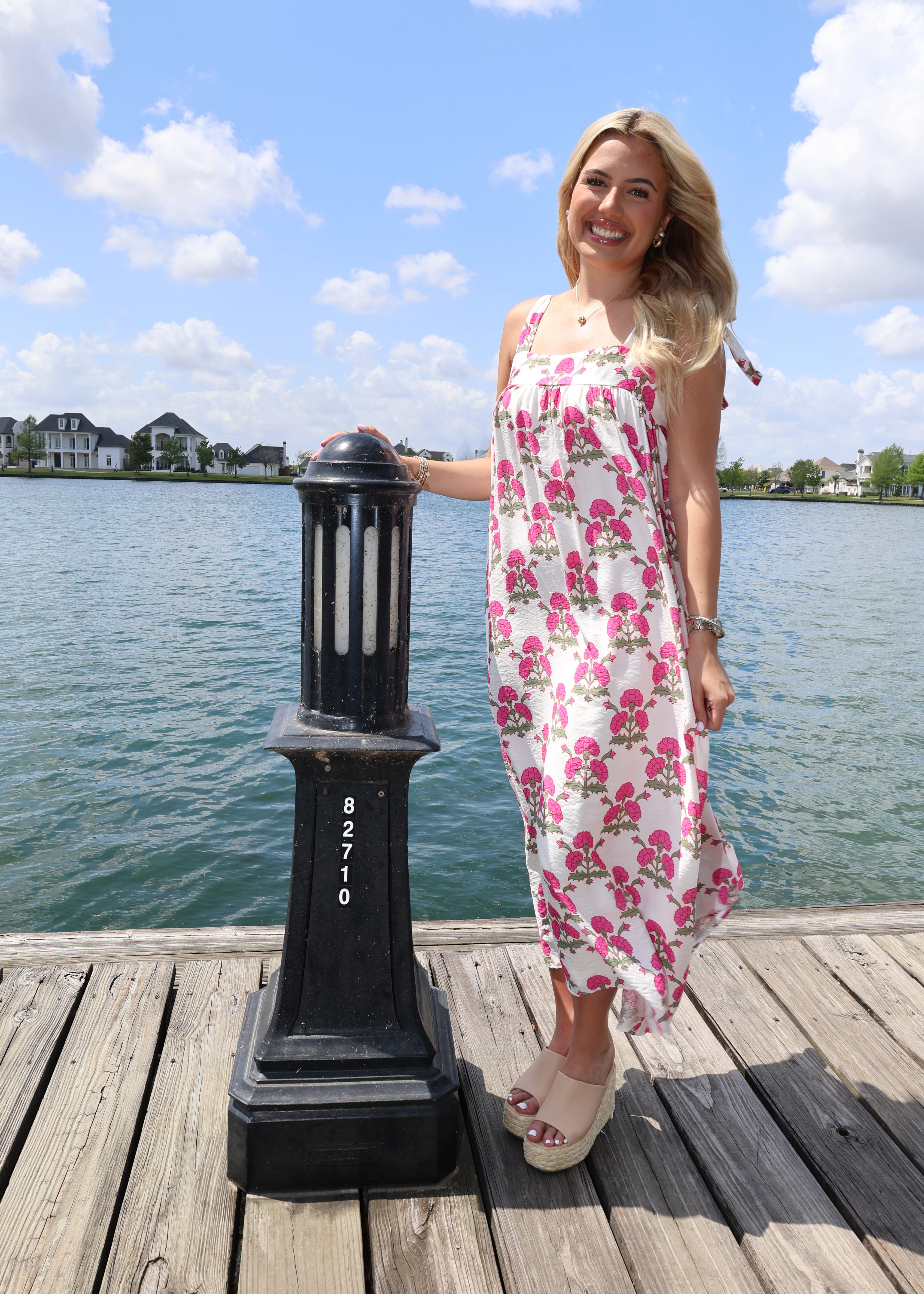 Woman in a floral dress standing on a dock with water and sky in the background