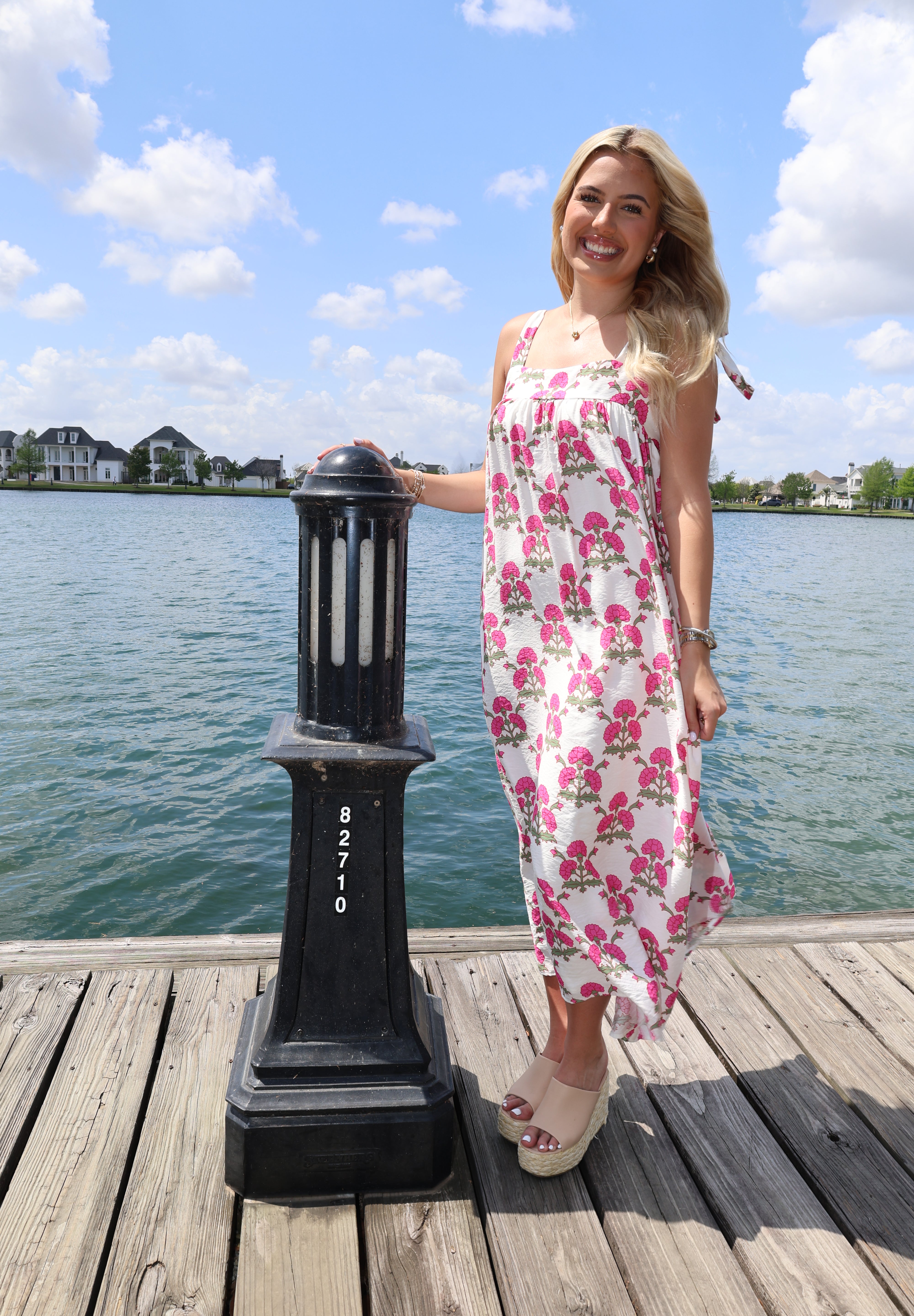 Woman in a floral dress standing on a dock with water and sky in the background