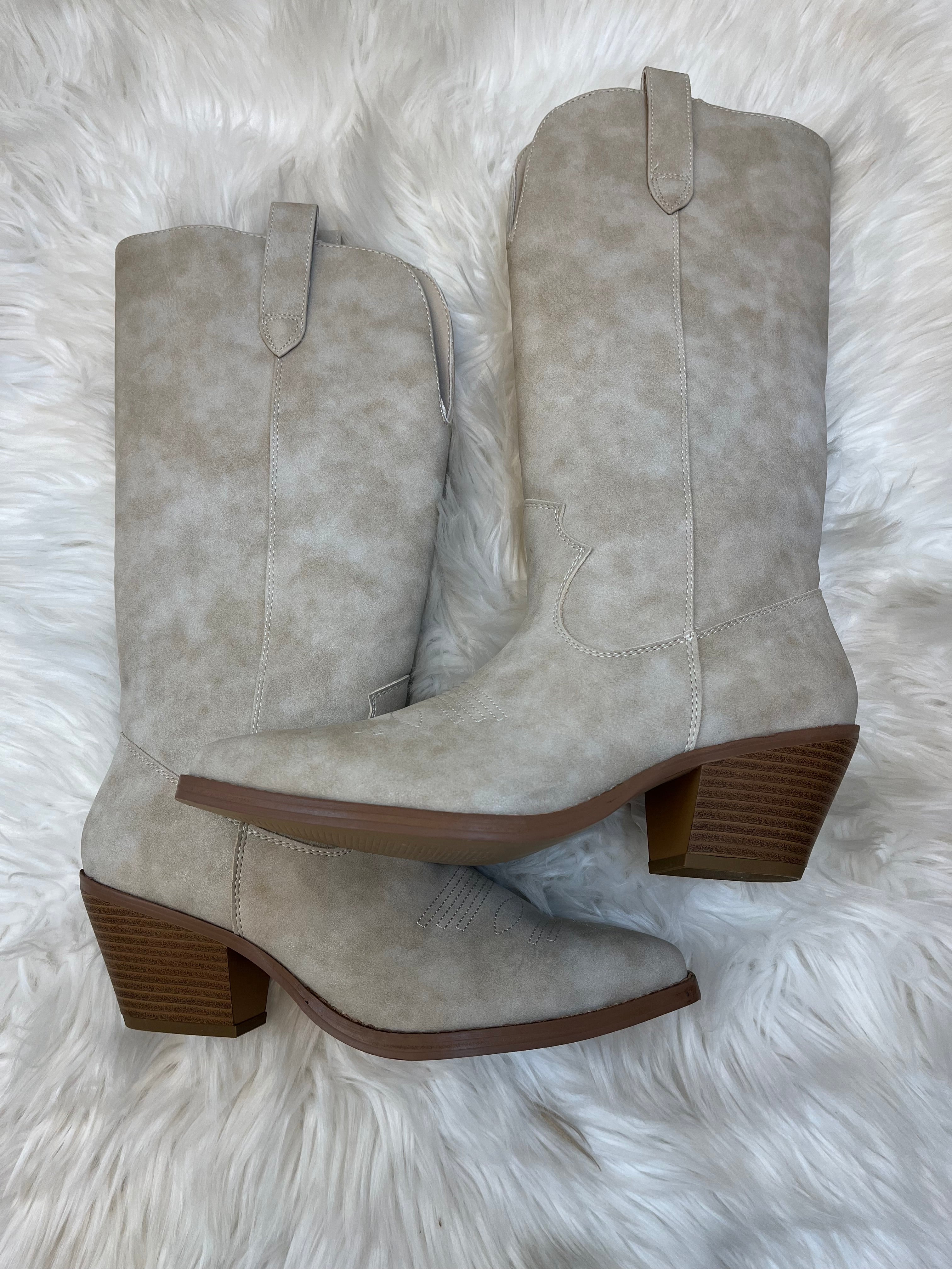 Pair of beige suede boots with brown soles on a white fluffy surface