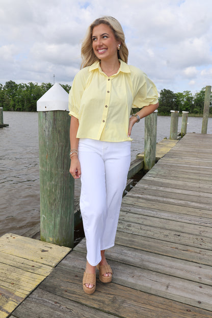 Woman in a yellow shirt and white pants standing on a wooden dock by a body of water.
